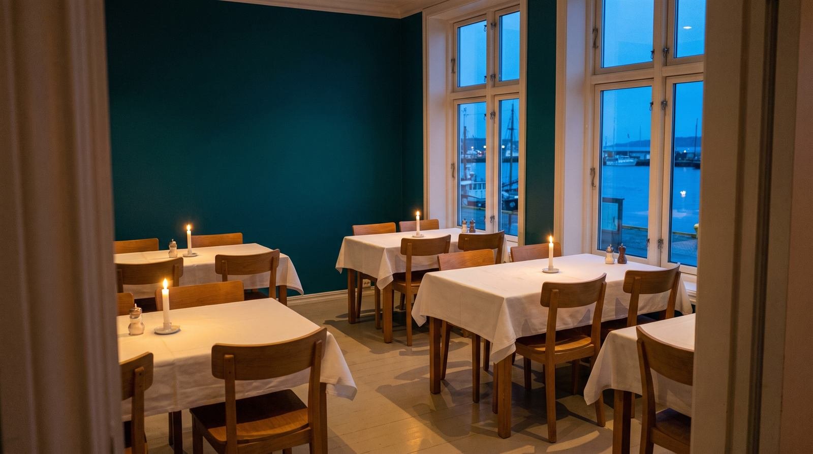 Comedor con mesas vestidas y velas, con el puerto al fondo